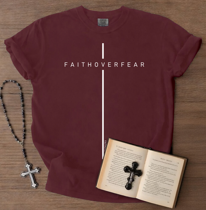 Maroon t-shirt with 'FAITHOVERFEAR' text, next to an open book with a cross and a rosary on a wooden surface.