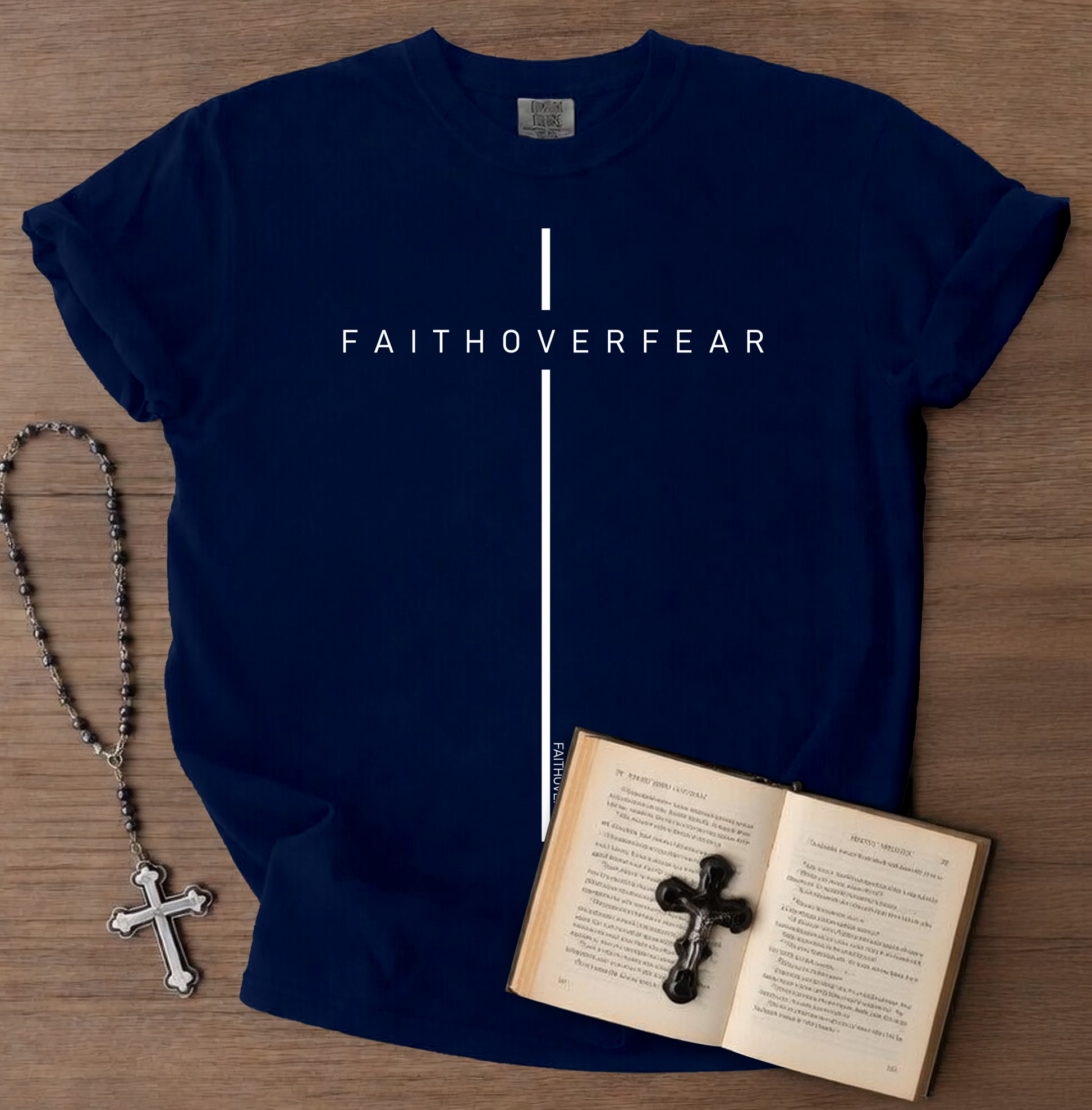 Navy blue t-shirt with 'FAITHOVERFEAR' text, rosary, and open book with cross on a wooden surface