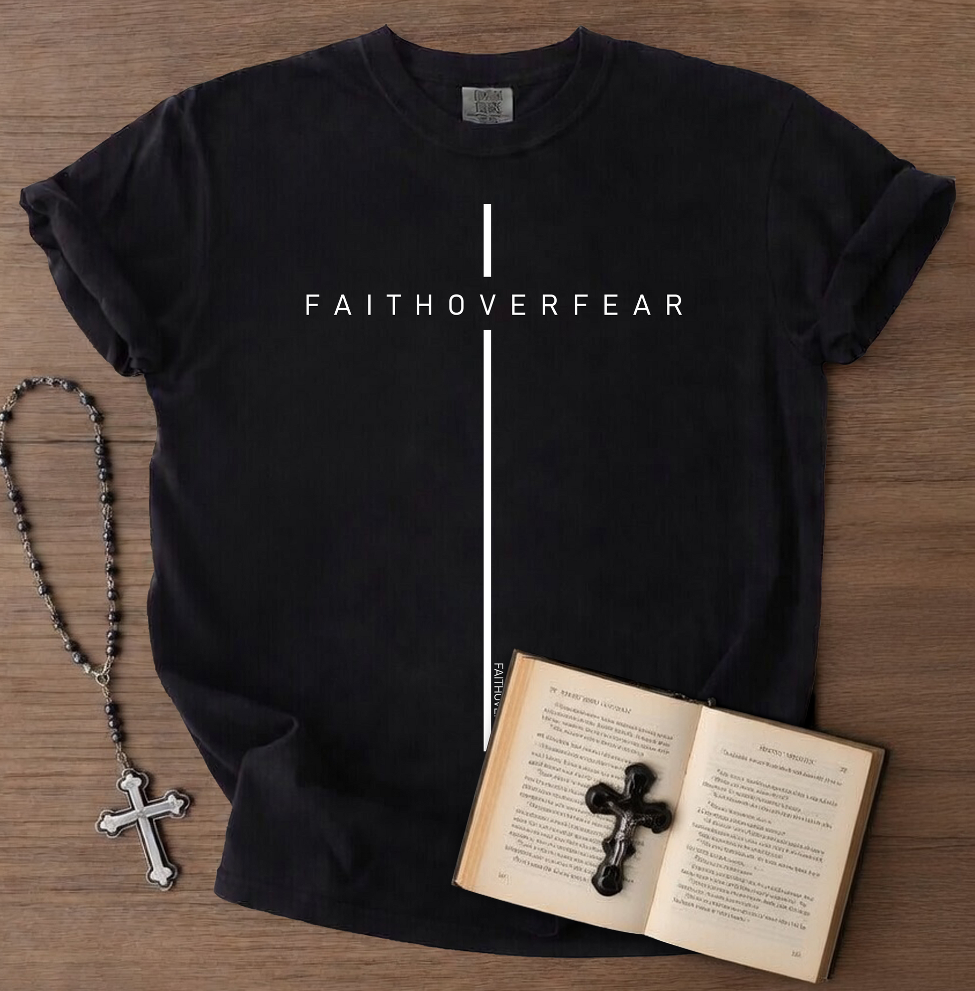 Black t-shirt with 'FAITHOVERFEAR' text, rosary, and open book on a wooden surface