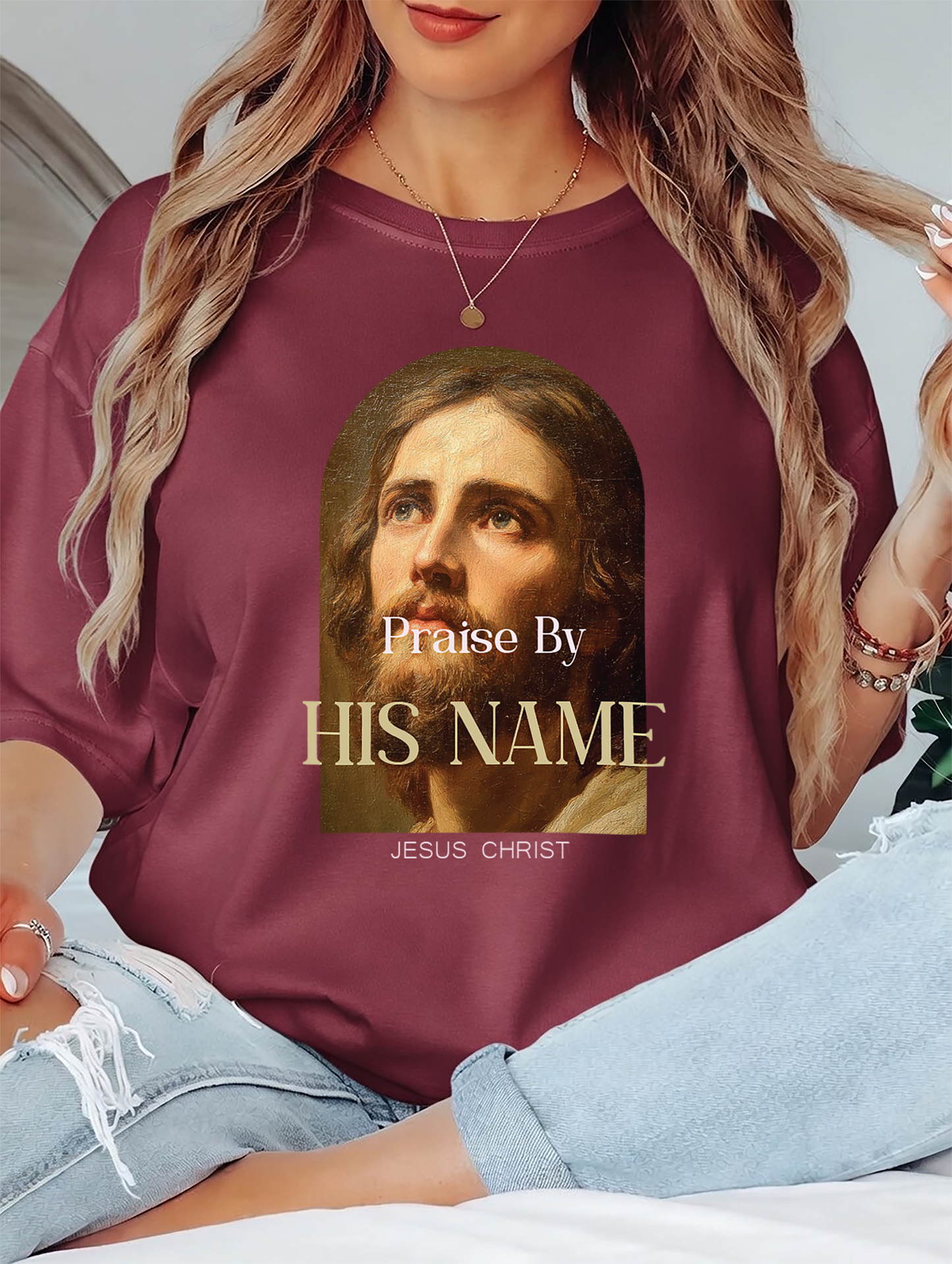 Person wearing a maroon sweatshirt with a graphic of Jesus Christ and text 'Praise By HIS NAME JESUS CHRIST'.