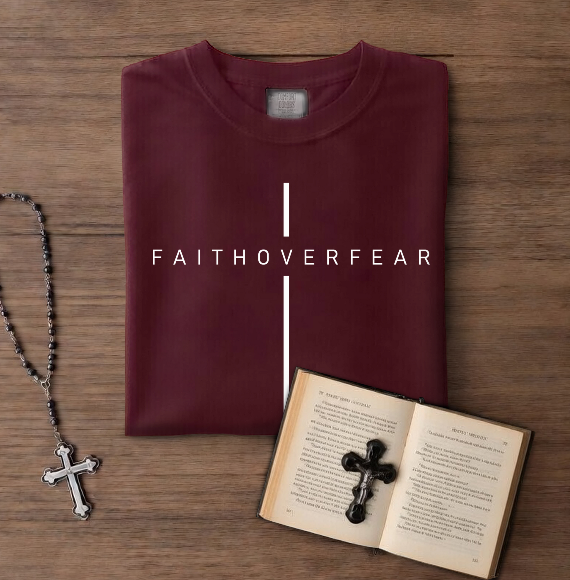 Maroon t-shirt with 'FAITHOVERFEAR' text, rosary, and open book with cross on wooden surface