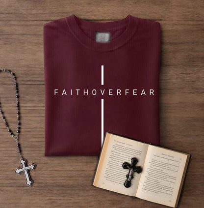 Maroon t-shirt with 'FAITHOVERFEAR' text, rosary, and open book with cross on wooden surface
